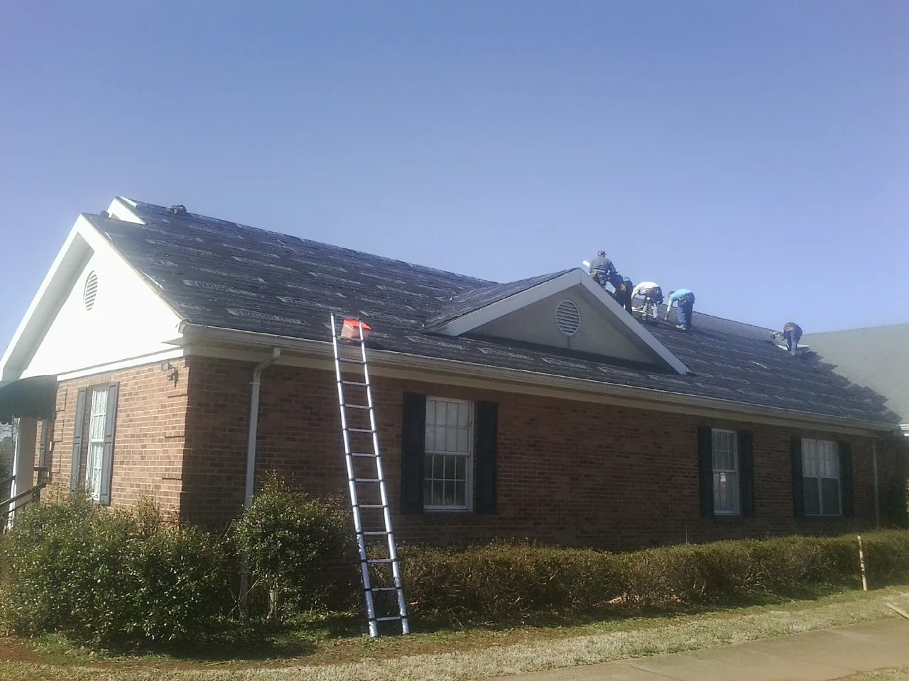 Crew tearing shingles off a brick ranch roof with a ladder set — Emergency Roof Repair work by our crew in Saint Louis
