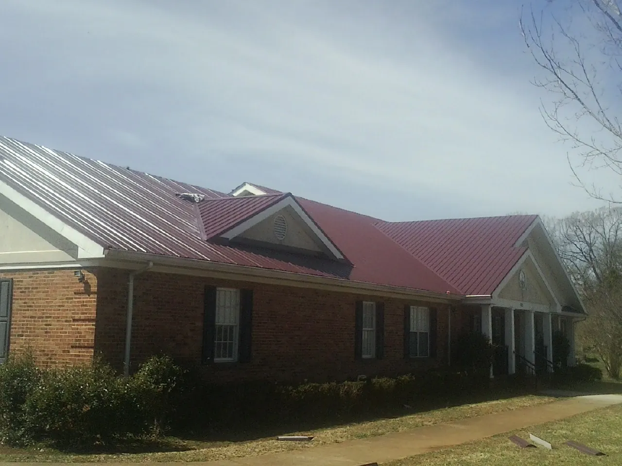 Red metal roof with gabled entries on a long brick building, from a Hail Damage Roof Repair job in Saint Louis