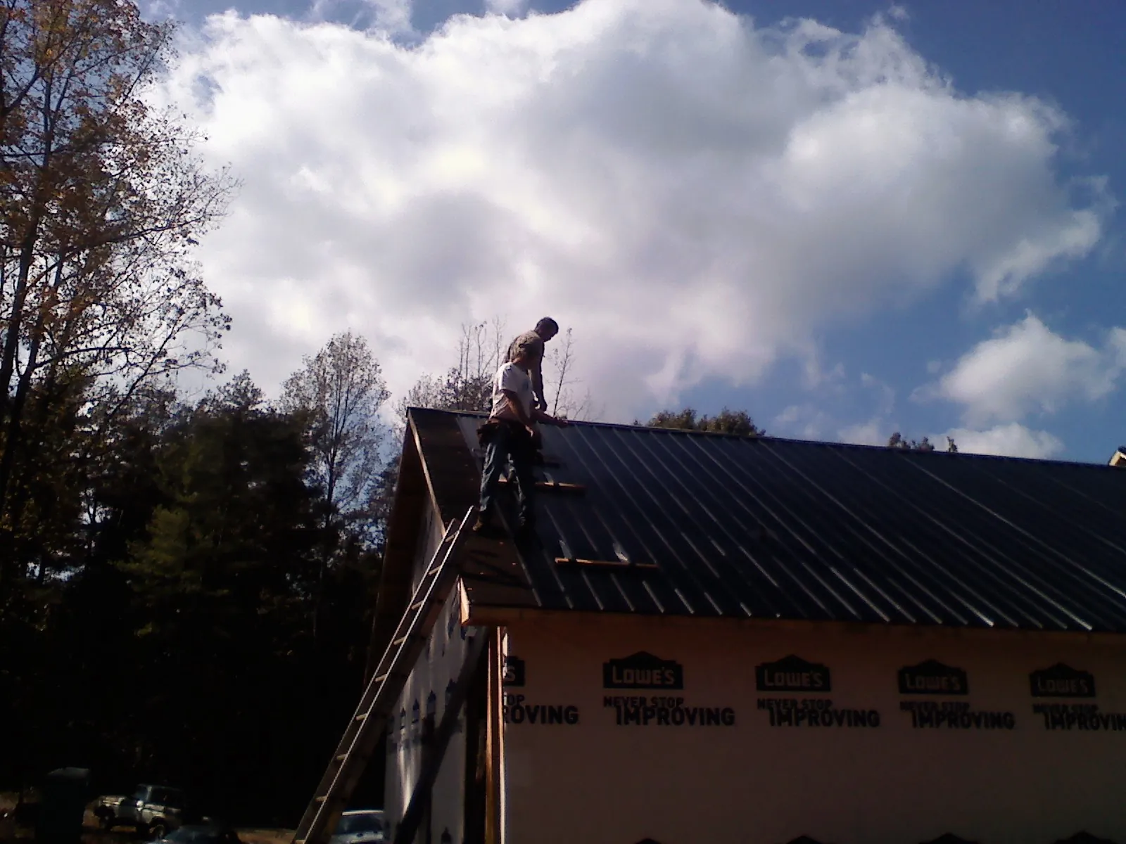 Roofer fastening dark metal panels high against a cloudy sky, from a Roof Inspection job in Saint Louis