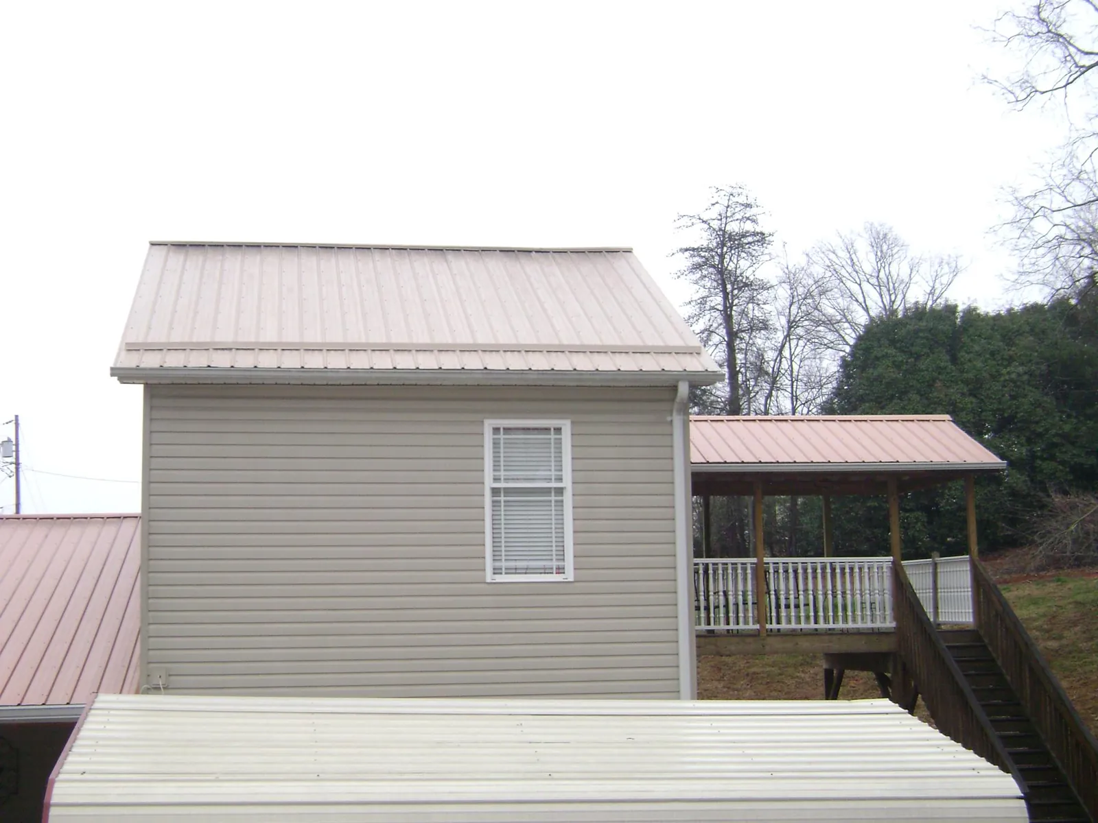 Tan metal roofs on a two story addition and attached porch, from a Roof Replacement job in Saint Louis
